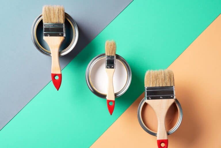 Metal paint cans and paint brushes on multicolor background. Top view. Copy space. Trendy green